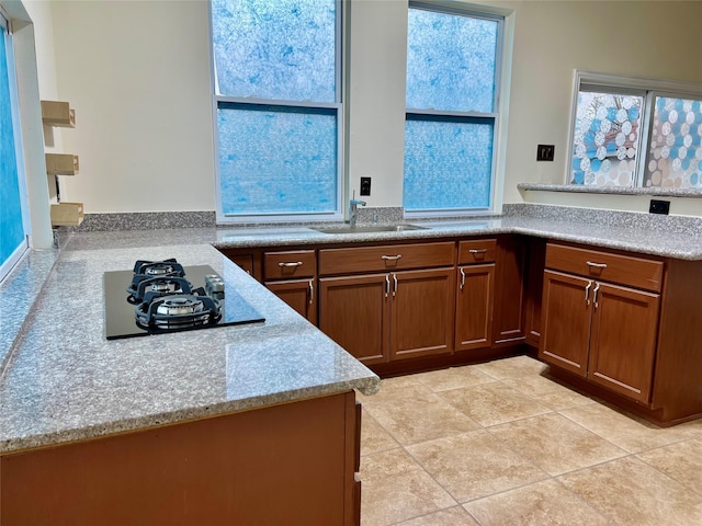 kitchen with black gas stovetop, a peninsula, a sink, light countertops, and brown cabinets