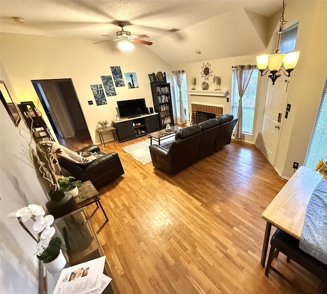 living room with a fireplace, lofted ceiling, visible vents, light wood-style flooring, and ceiling fan