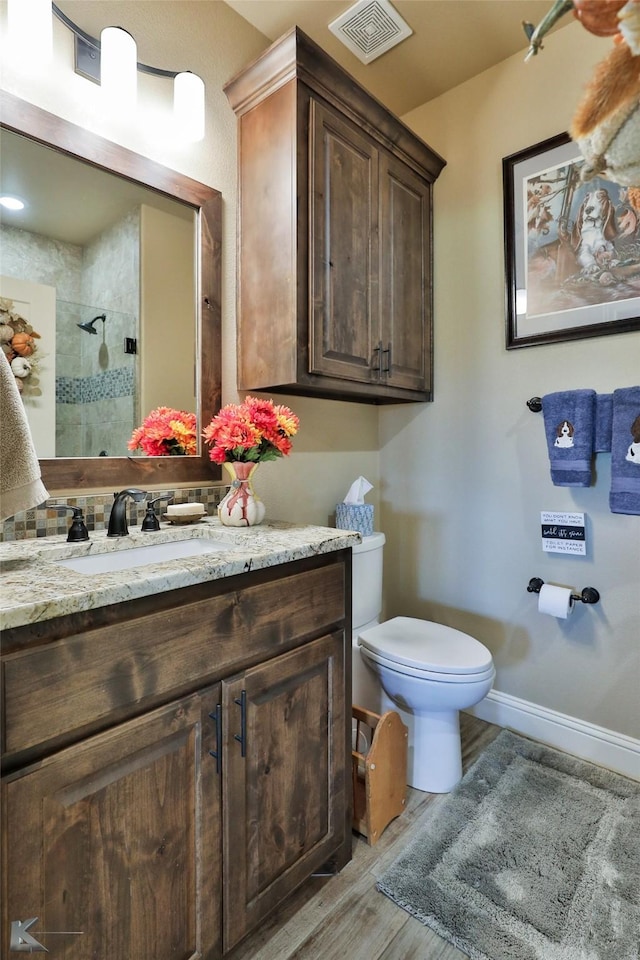 bathroom with vanity, wood-type flooring, a tile shower, and toilet