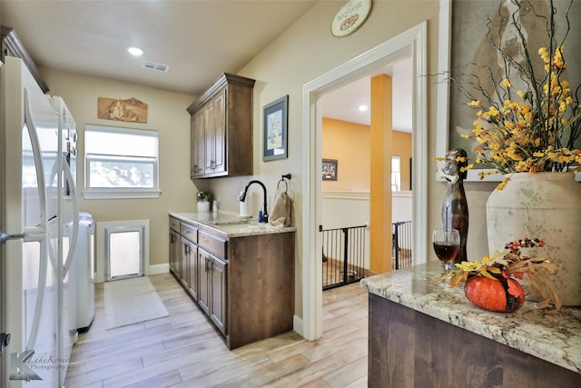 kitchen featuring white refrigerator, light stone counters, dark brown cabinets, and light wood-type flooring