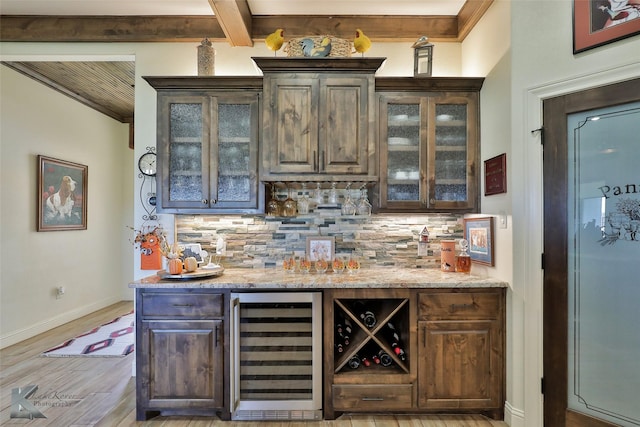 bar with wine cooler, decorative backsplash, dark brown cabinetry, light stone countertops, and beam ceiling