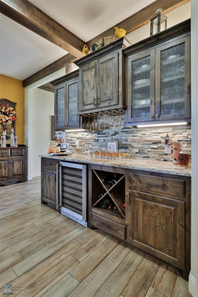 bar featuring light wood-type flooring, beverage cooler, backsplash, dark brown cabinets, and beam ceiling