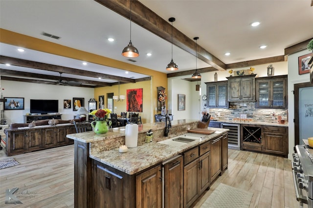 kitchen featuring an island with sink, backsplash, high end stainless steel range oven, hanging light fixtures, and dark brown cabinetry