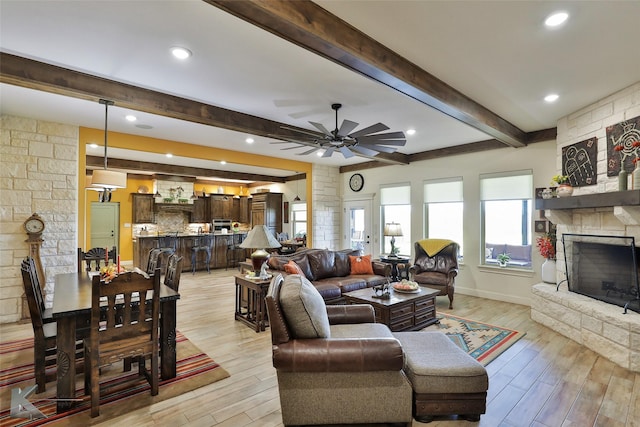 living room featuring beamed ceiling, a stone fireplace, ceiling fan, and light hardwood / wood-style flooring