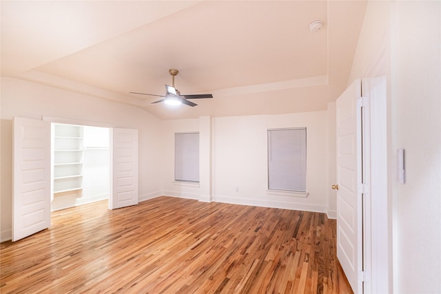 unfurnished bedroom featuring a walk in closet, ceiling fan, lofted ceiling, and light wood-type flooring