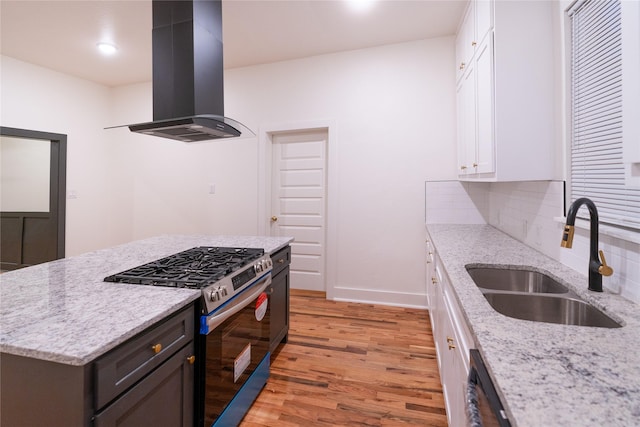 kitchen with sink, gas stove, white cabinetry, island range hood, and light stone countertops