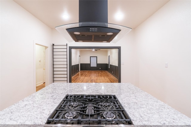 kitchen with gas stovetop, light wood-type flooring, island range hood, and light stone counters