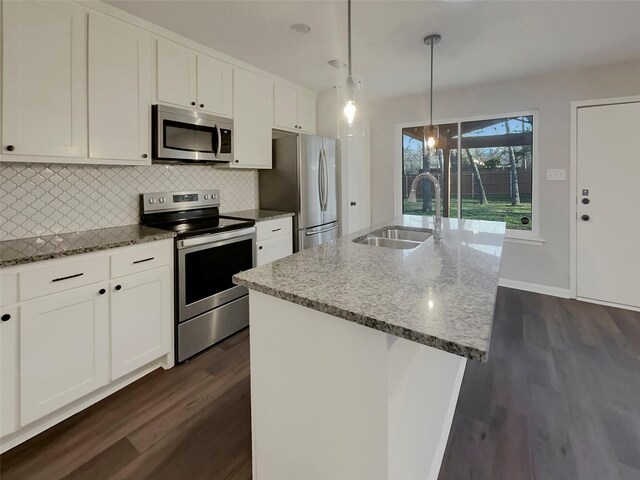 kitchen with sink, a kitchen island with sink, dark stone countertops, stainless steel appliances, and decorative light fixtures