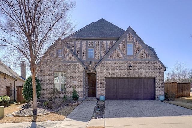 view of front of house featuring roof with shingles, brick siding, decorative driveway, and fence