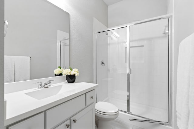 bathroom featuring a stall shower, a textured wall, vanity, and toilet