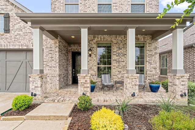 property entrance with covered porch, brick siding, and a garage