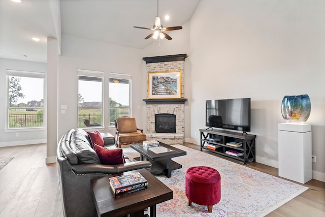 living room with a brick fireplace, baseboards, light wood finished floors, and a ceiling fan