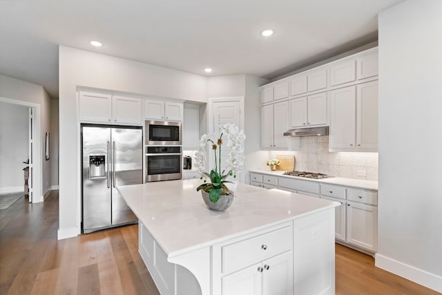 kitchen with tasteful backsplash, stainless steel appliances, light countertops, light wood-type flooring, and under cabinet range hood