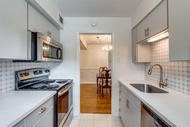 kitchen featuring sink, gray cabinets, backsplash, stainless steel appliances, and a notable chandelier