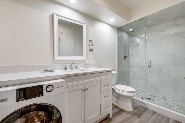 bathroom featuring a shower with door, hardwood / wood-style floors, vanity, washer / clothes dryer, and toilet