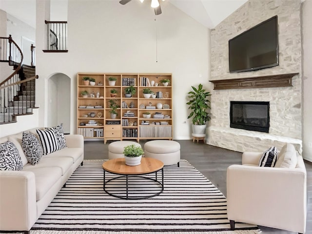 living room featuring a stone fireplace, wood-type flooring, high vaulted ceiling, and ceiling fan