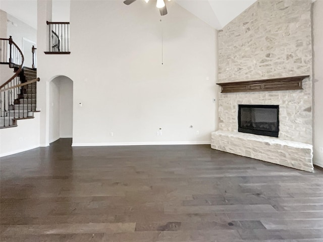 unfurnished living room with a stone fireplace, high vaulted ceiling, dark hardwood / wood-style floors, and ceiling fan