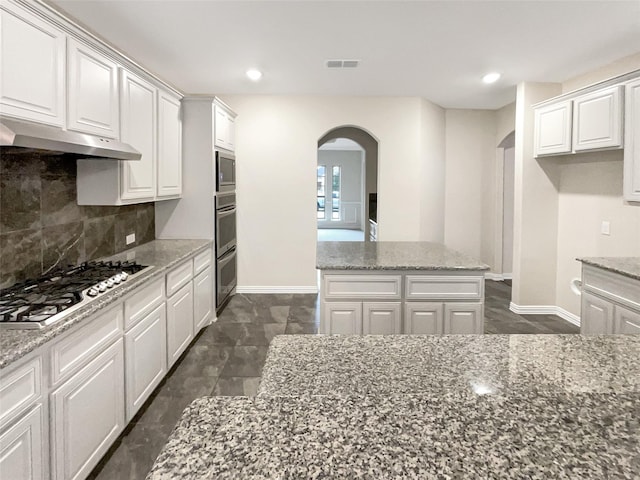 kitchen featuring appliances with stainless steel finishes, a kitchen island, white cabinetry, decorative backsplash, and light stone countertops