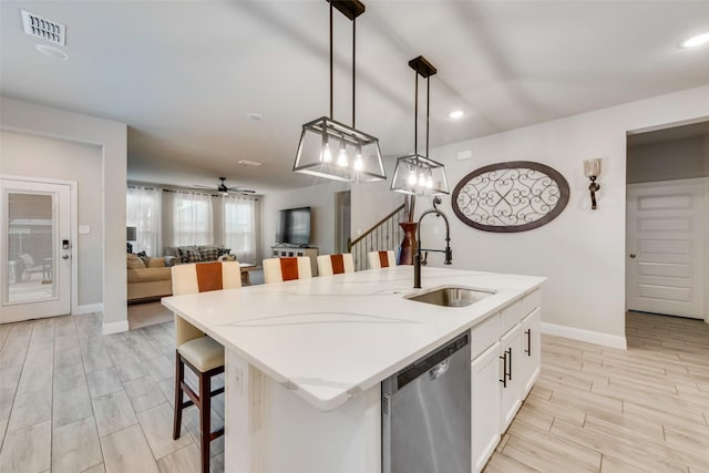 kitchen featuring sink, dishwasher, an island with sink, a kitchen bar, and decorative light fixtures