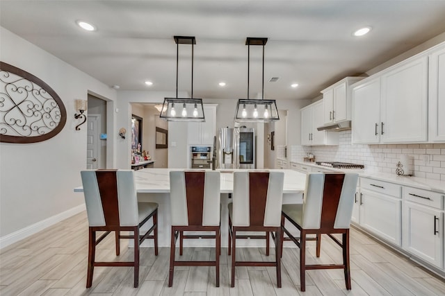 kitchen featuring tasteful backsplash, decorative light fixtures, a kitchen island, stainless steel appliances, and white cabinets