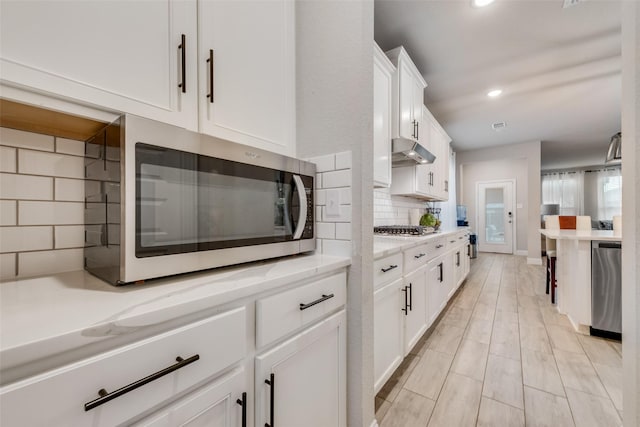 kitchen featuring stainless steel appliances, light stone countertops, white cabinets, and decorative backsplash