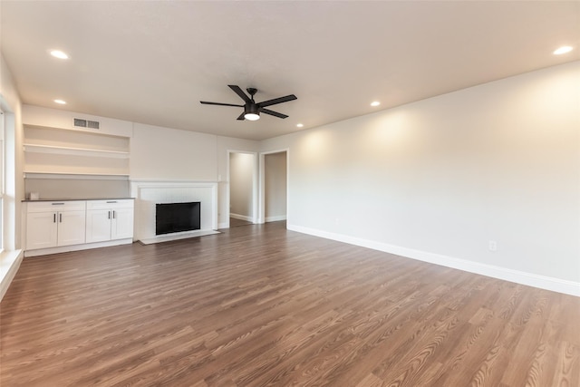 unfurnished living room featuring built in shelves, ceiling fan, and hardwood / wood-style floors