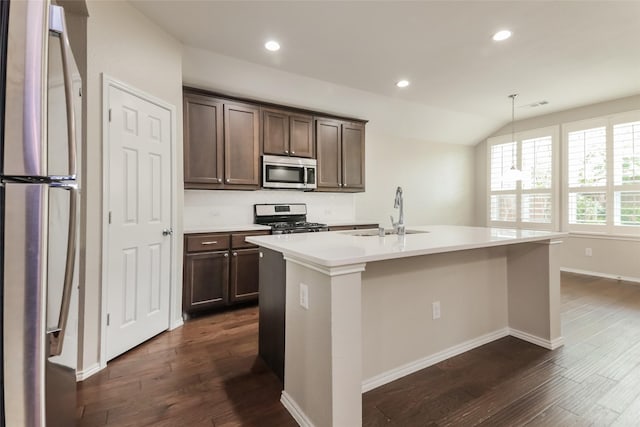 kitchen with appliances with stainless steel finishes, decorative light fixtures, an island with sink, sink, and dark wood-type flooring