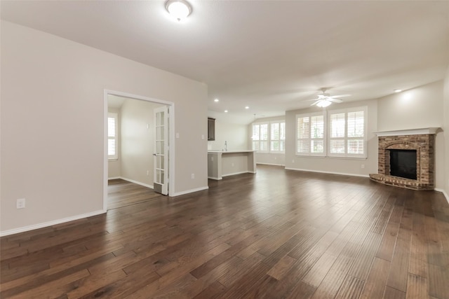 unfurnished living room with a brick fireplace, a wealth of natural light, dark hardwood / wood-style floors, and ceiling fan