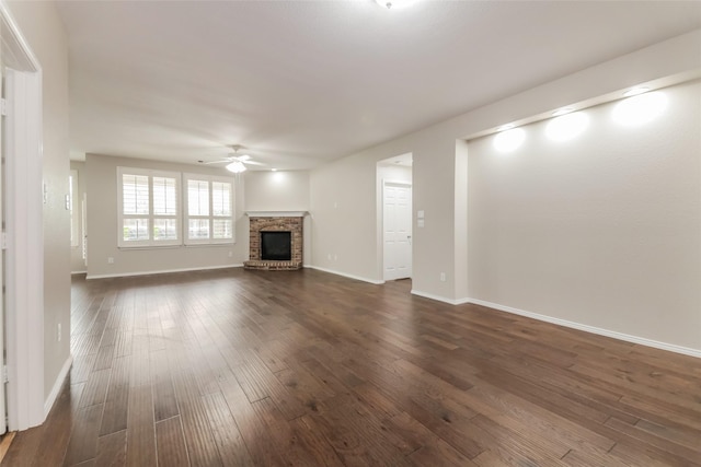 unfurnished living room with a brick fireplace, dark wood-type flooring, and ceiling fan