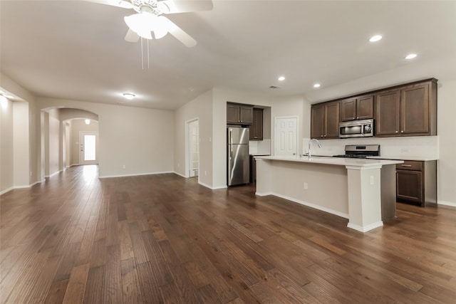 kitchen featuring sink, dark brown cabinets, stainless steel appliances, dark hardwood / wood-style floors, and a center island with sink