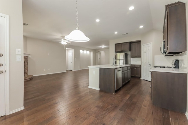 kitchen featuring a kitchen island with sink, hanging light fixtures, dark wood-type flooring, and stainless steel appliances