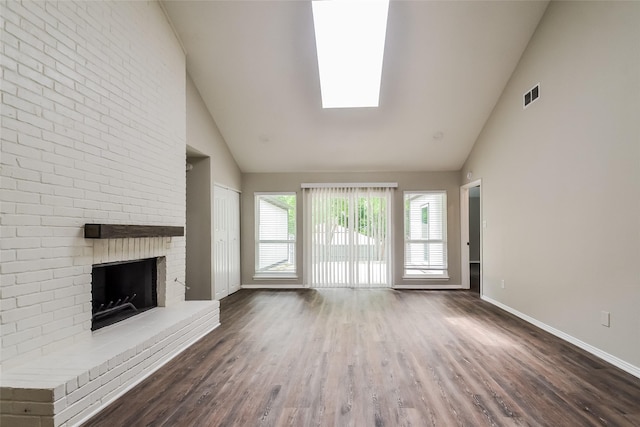 unfurnished living room featuring a brick fireplace, high vaulted ceiling, dark hardwood / wood-style flooring, and a skylight