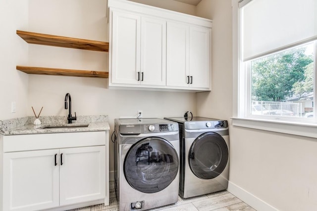 laundry area featuring cabinets, sink, washing machine and clothes dryer, and light hardwood / wood-style floors