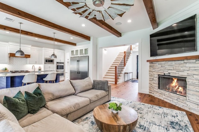 living room with ceiling fan, beam ceiling, a fireplace, and light wood-type flooring