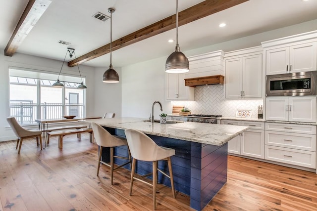 kitchen with sink, decorative light fixtures, stainless steel microwave, a kitchen island with sink, and white cabinets