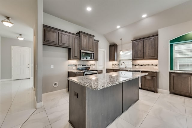 kitchen featuring sink, light stone counters, a center island, appliances with stainless steel finishes, and backsplash