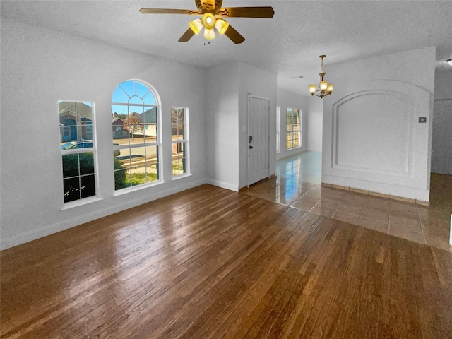 unfurnished living room featuring hardwood / wood-style flooring, ceiling fan with notable chandelier, and a textured ceiling