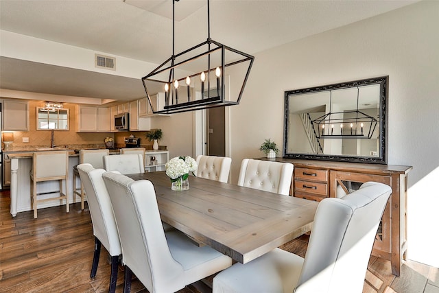 dining area featuring sink, dark wood-type flooring, and a chandelier