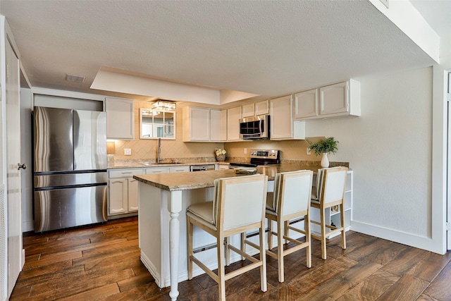 kitchen featuring sink, appliances with stainless steel finishes, dark hardwood / wood-style floors, white cabinets, and a kitchen bar