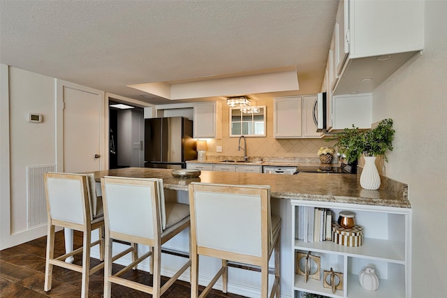 kitchen with sink, a breakfast bar area, white cabinetry, stainless steel appliances, and tasteful backsplash