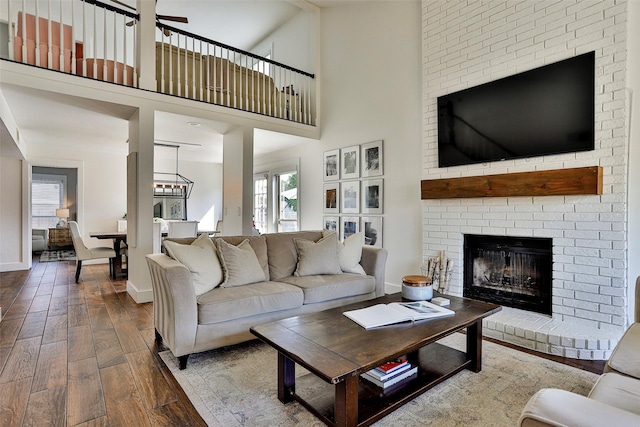 living room with ceiling fan, wood-type flooring, a fireplace, and a high ceiling