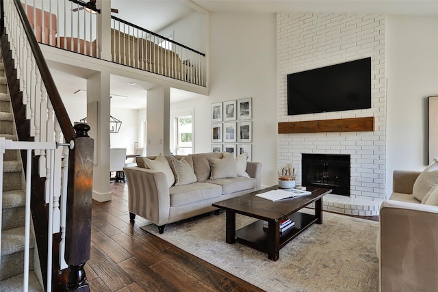 living room featuring a towering ceiling, a fireplace, dark hardwood / wood-style floors, and ceiling fan