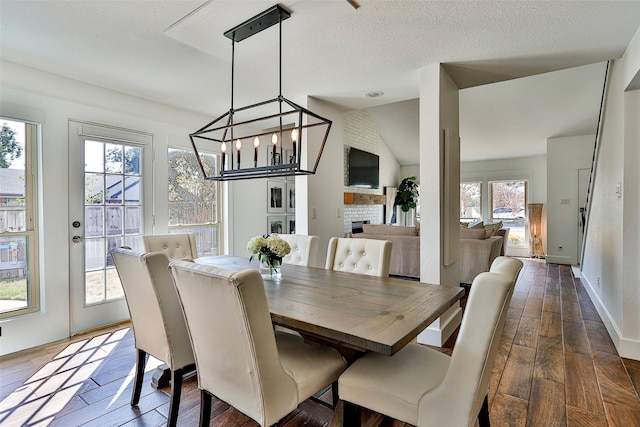 dining room with a chandelier, vaulted ceiling, a textured ceiling, dark hardwood / wood-style floors, and a fireplace