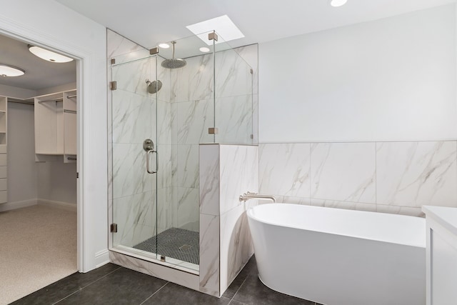 bathroom featuring a skylight, tile walls, vanity, plus walk in shower, and tile patterned flooring