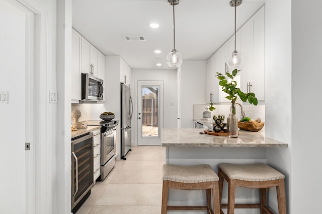 kitchen with appliances with stainless steel finishes, white cabinetry, a kitchen breakfast bar, kitchen peninsula, and light stone countertops