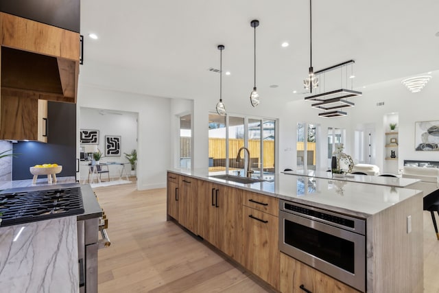 kitchen featuring a large island, sink, light hardwood / wood-style flooring, light stone countertops, and decorative light fixtures