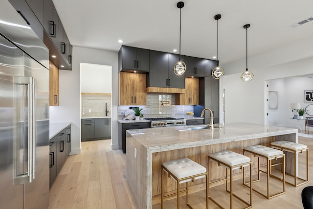 kitchen featuring light stone countertops, high quality fridge, an island with sink, a kitchen bar, and decorative light fixtures