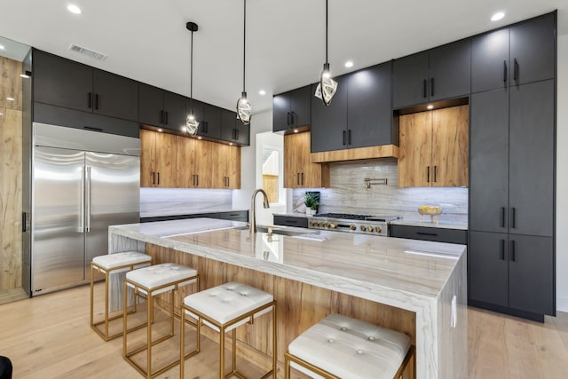 kitchen with sink, a kitchen bar, a center island with sink, decorative light fixtures, and built in fridge