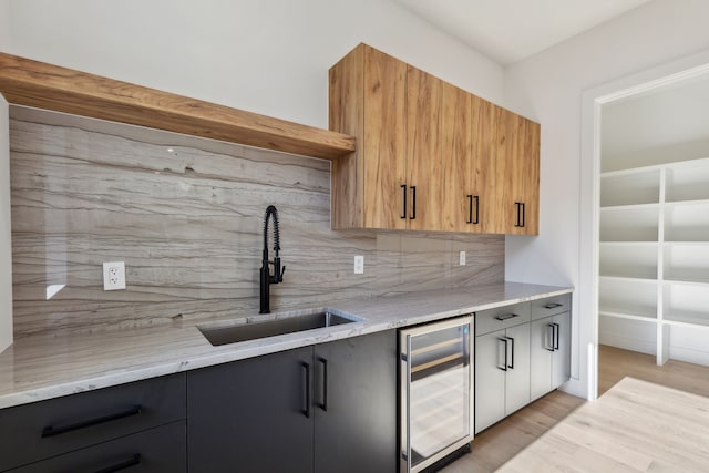 kitchen featuring sink, tasteful backsplash, light stone countertops, light hardwood / wood-style floors, and beverage cooler