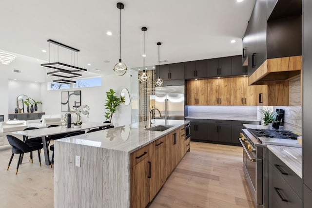 kitchen with a large island, sink, light stone counters, premium appliances, and decorative light fixtures